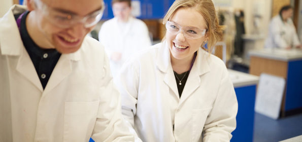 Two students smile and work together in a science lab with lab coats on in Hartlepool Sixth Form