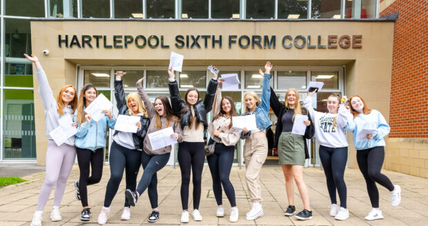 A group of students, holding their GCSE results, smile in front of the Hartleepool Sixth Form building.